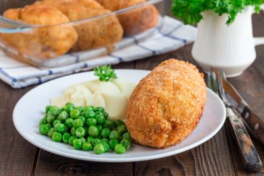 Tavuk Kiev, Ukrayna mutfağı. Tereyağı ve otla doldurulmuş ekmek kırıntıları içinde tavuk pirzolası, patates püresi ve yeşil bezelyeyle servis edilmiş, beyaz bir tabakta, yatay olarak.