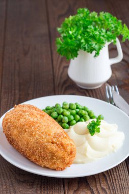 Tavuk Kiev, Ukrayna mutfağı. Tereyağı ve otla doldurulmuş ekmek kırıntıları içinde tavuk pirzolası, patates püresi ve yeşil bezelye ile servis edilmiş, beyaz bir tabakta, dikey