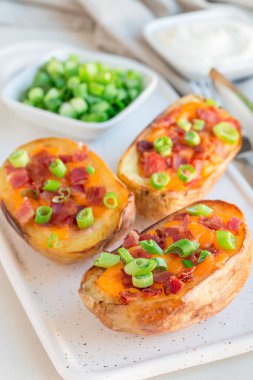 Çedar peyniri ve pastırmalı fırında patates kabuğu seramik tabakta, soğan ve ekşi kremayla süslenmiş, dikey.