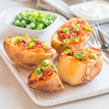 Seramik tabakta çedar peyniri ve pastırmalı fırında patates kabuğu, soğan ve ekşi kremayla süslenmiş, kare şeklinde.