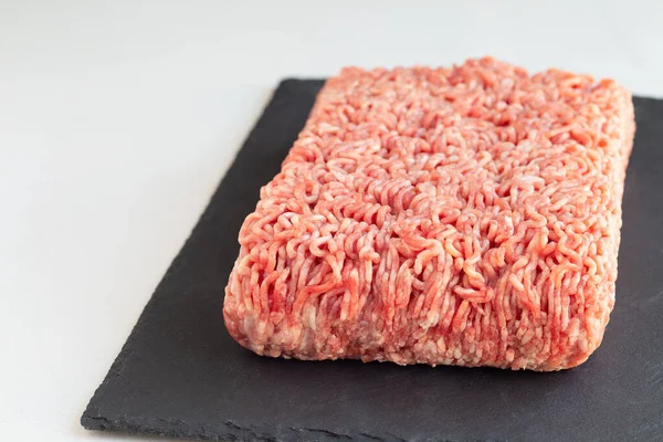 Minced meat from pork and beef, ground meat on a dark slate board, horizontal, copy space