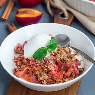 Erikli turta veya yulaf ve baharatlı erik gevreği, vanilyalı dondurma topu ile servis edilir, beyaz bir tabakta, kare şeklinde.