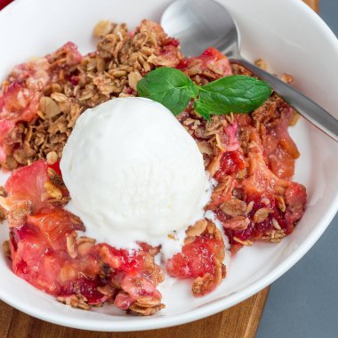 Erikli turta veya yulaf ve baharatlı erik gevreği, vanilyalı dondurma topu ile servis edilir, beyaz tabakta, kare formatta, yakın plan.