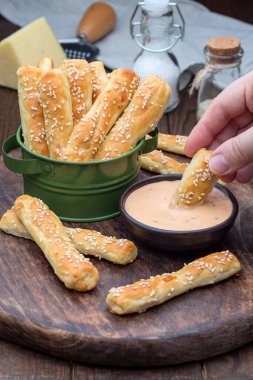 Peynirli ve susamlı ev yapımı lezzetli ekmek çubukları, ahşap bir tahtada sosla servis ediliyor, dikey.