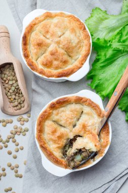 Mercimek, mantar, patates, havuç ve yeşil bezelyeyle kaplı vejetaryen turtası, kabartma tabağı, dikey, üst görünüm