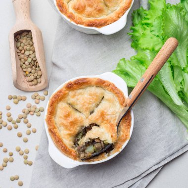 Mercimek, mantar, patates, havuç ve yeşil bezelyeyle kaplı vejetaryen turtası, kabartma tabağında, kare şeklinde, üst görünümde.