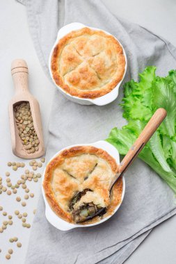 Mercimek, mantar, patates, havuç ve yeşil bezelyeyle kaplı vejetaryen turtası, kabartma kabında, dikey, üst görünümde.