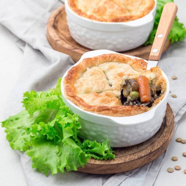 Mercimek, mantar, patates, havuç ve yeşil bezelyeyle kaplı vejetaryen turtası, kabartma tabağında, kare