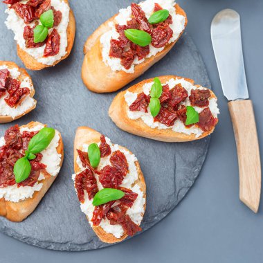 Güneşte kurutulmuş domates, feta ve Philadelphia peyniri ve fesleğenle taş bir tabakta, üst manzara, kare, yakın çekim