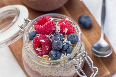 Kavanozda katmanlı çikolata ve fıstık ezmeli chia tohumu pudingi, ahududu, yabanmersini, bal ve hindistan cevizi taneleri ile süslenmiş, yatay, yakın plan