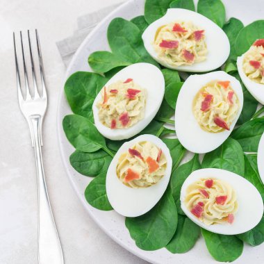 Avokado, yumurta sarısı ve mayonez ile doldurulmuş yumurta, pastırmayla süslenmiş ıspanak yaprakları, üst görünüm, kare şeklinde.
