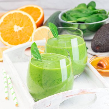 Tahta bir tepside, avokado, ıspanak, salatalık, portakal, limon ve bal ile yeşil detoks smoothie, kare format