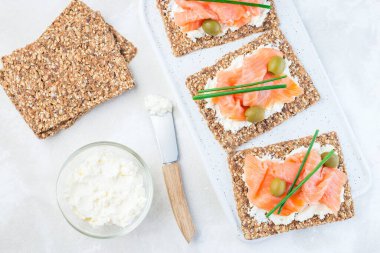 Füme somon ve krem peynirli sandviç ince çok tohumlu cips, yeşil soğan ve zeytinlerle süslenmiş, yatay, üst görünüm