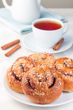 Beyaz tabakta tarçınlı çörekler, bir fincan kırmızı çay ile servis edilir, dikey.