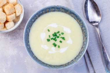 Patates püresi çorbası mavi bir seramik kasede Fransız kreması ve yeşil soğanla süslenmiş, kıtır ekmeklerle servis edilmiş, yatay, üst manzara