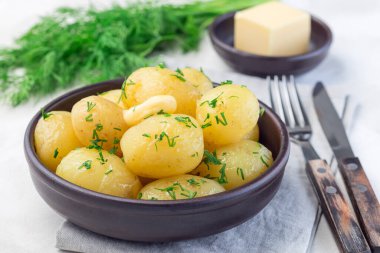 New young boiled potato topped with melted butter and chopped dill in a ceramic bowl, horizontal clipart