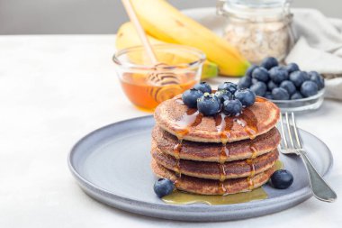 Sağlıklı yulaf ezmeli muzlu krep yabanmersini ve bal ile süslenmiş gri bir tabakta, yatay, kopyalama alanı
