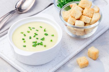 Beyaz bir seramik kasede yeşil soğanla süslenmiş patates püresi çorbası.