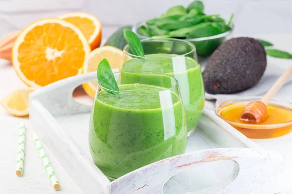 Ahşap tepside, avokado, ıspanak, salatalık, portakal, limon ve bal içeren yeşil detoks smoothie.