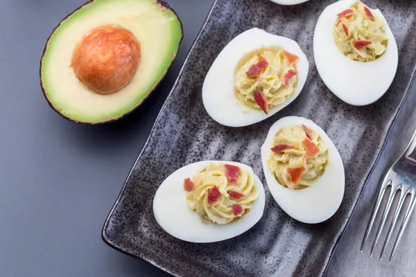 Avokado, yumurta sarısı ve mayonez ile doldurulmuş yumurtalar, pastırmayla süslenmiş, yatay, üst manzara