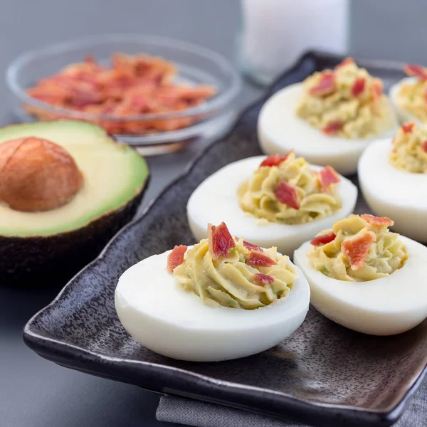 Avokado, yumurta sarısı ve mayonez ile doldurulmuş yumurta, pastırmayla süslenmiş, kare şeklinde.