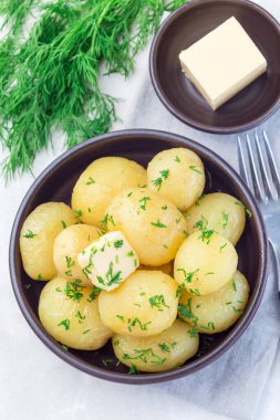 New young boiled  potato topped with melted butter and chopped dill in a ceramic bowl, vertical,  top view clipart