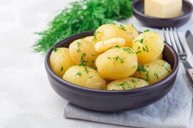 New young boiled  potato topped with melted butter and chopped dill in a ceramic bowl, horizontal, copy space clipart