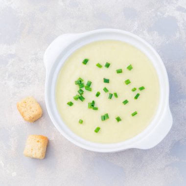 Patates püresi çorbası beyaz seramik kasede yeşil soğanla süslenmiş, kızarmış ekmeklerle servis edilmiş, üst manzara, kare format