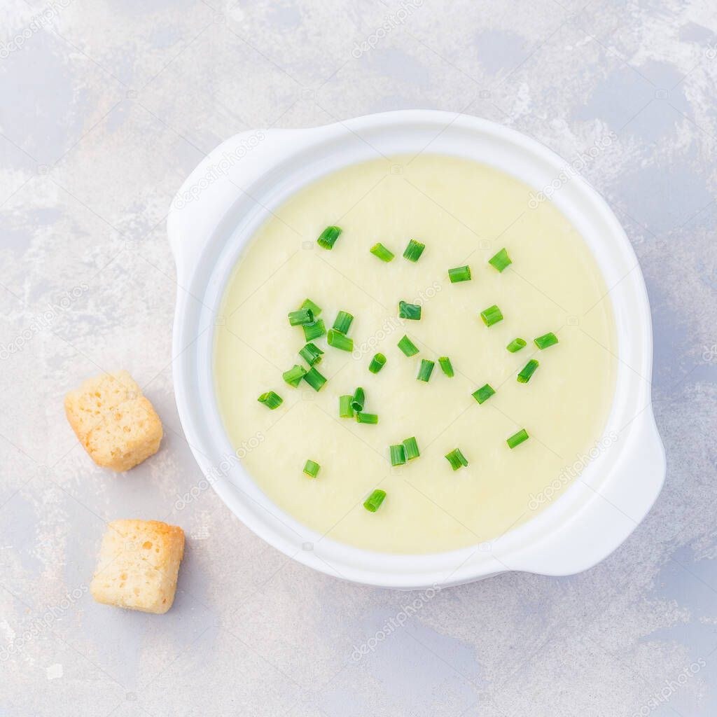 Potato leek soup in white ceramic bowl garnished with green onion, served with croutons, top view,  square format