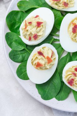 Avokado, yumurta sarısı ve mayonez ile doldurulmuş yumurta, pastırmayla süslenmiş ıspanak yaprakları, dikey, üst manzara, yakın çekim.