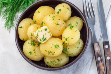 New young boiled  potato topped with melted butter and chopped dill in a ceramic bowl, horizontal,  top view clipart