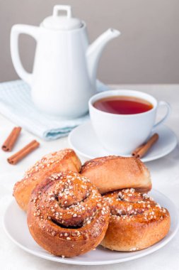 Beyaz tabakta tarçınlı çörekler, bir fincan kırmızı çay ile servis edilir, dikey.