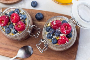 Kavanozda çikolata ve fıstık ezmeli chia tohumu pudingi, ahududu, yabanmersini, bal ve hindistan cevizi taneleri ile süslenmiş, yatay, üst manzara