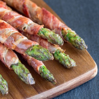 Sağlıklı aperatif, ahşap tahtaya sarılı yeşil kuşkonmaz, kare şeklinde.