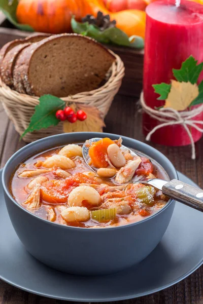 Soup with turkey, pasta, carrot, celery, tomato and cannellini beans, garnished with parmesan cheese, on the table with autumn decoration, reflecting the US Thanksgiving harvest feast, vertical,  closeup