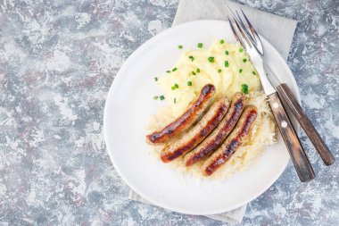 Kızarmış nuremberg sosisleri ekşi lahana ve patates püresi ile servis edilir, beyaz bir tabakta, yatay, üst manzara, kopyalama alanı