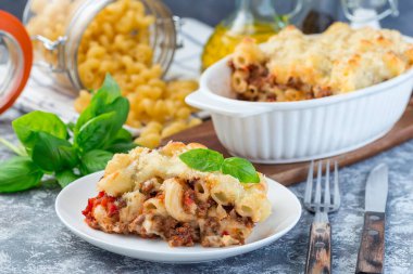 Beyaz tabakta kıymalı, peynirli ve domatesli makarna güveci.