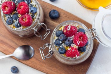 Kavanozda çikolata ve fıstık ezmeli chia tohumu pudingi, ahududu, yabanmersini, bal ve hindistan cevizi taneleri ile süslenmiş, yatay, üst görünüm