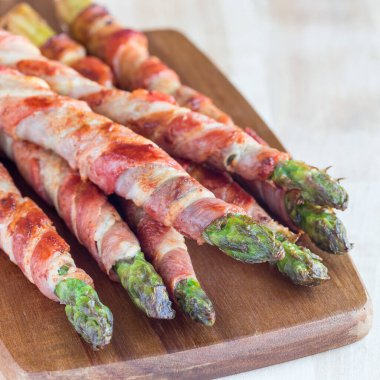 Sağlıklı aperatif, ahşap bir tahtaya sarılı yeşil kuşkonmaz, kare şeklinde.