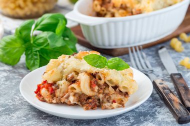 Beyaz tabakta kıymalı, peynirli ve domatesli makarna güveci, yatay, yakın plan.