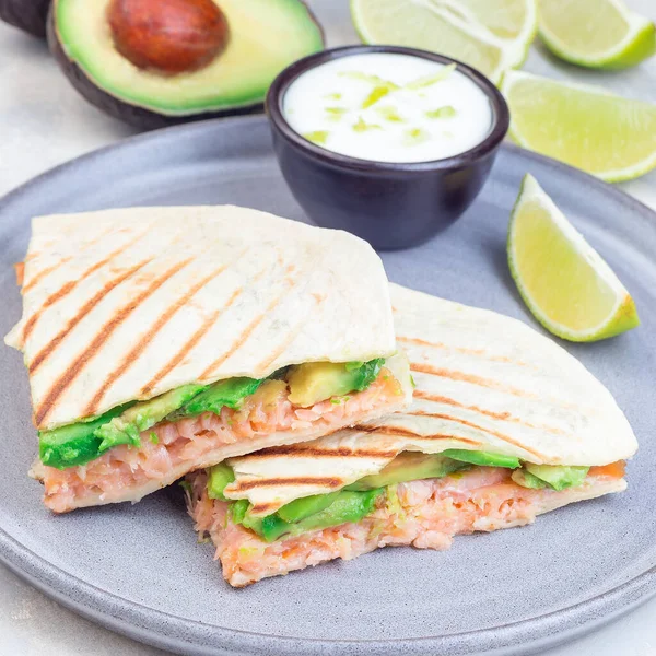 Grilled quesadilla with smoked salmon and avocado served with yogurt and lime dip, on a gray plate, square format, closeup