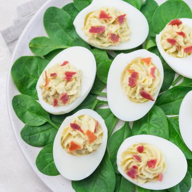 Avokado, yumurta sarısı ve mayonez ile doldurulmuş yumurta, pastırmayla süslenmiş ıspanak yaprakları, üst manzara, kare