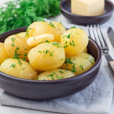 New young boiled potato topped with melted butter and chopped dill in a ceramic bowl, square format clipart