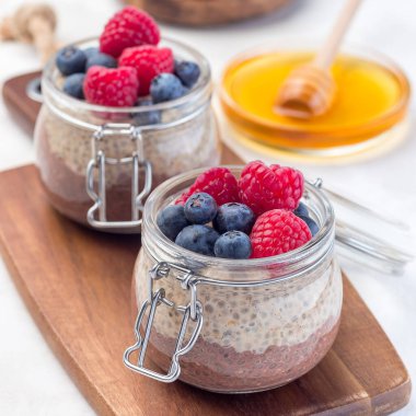 Kavanozda çikolata ve fıstık ezmeli chia tohumu pudingi, ahududu ve yaban mersiniyle süslenmiş, kare şeklinde.