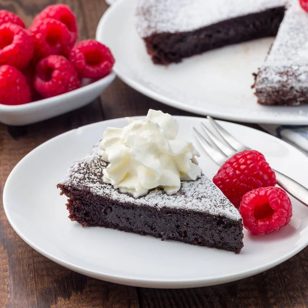 チョコレートの粘りのあるブラウニーケーキ スウェーデンのデザートKladdkaka プレート上に アイシングシュガーとラズベリーを添えて 正方形のフォーマット — ストック写真