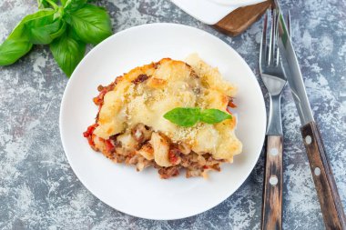 Beyaz tabakta kıymalı, peynirli ve domatesli makarna güveci.