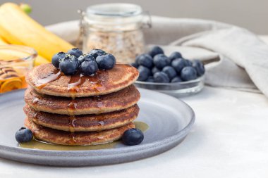 Sağlıklı yulaf ezmeli muzlu krep yabanmersini ve bal ile süslenmiş gri tabakta, yatay, kopyalama alanı