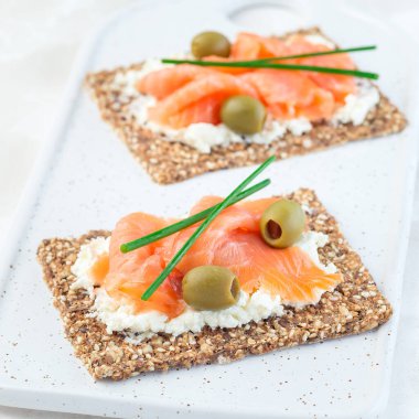 Taze soğan ve zeytinle süslenmiş ince çoklu tohum ekmeğine füme somon ve krem peynirli sandviç.