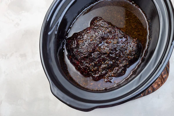 Pork shoulder in honey parmesan and soy souse, prepared in slow cooker or crockpot, in a slow cooker pot, top view, horizontal, copy space