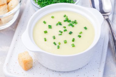 Patates püresi çorbası beyaz bir seramik kasede yeşil soğanla süslenmiş kıtır ekmeklerle servis edilmiş, yatay ve yakın plan.